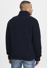 Marineblå fleece-pullover med høy krage, teksturert overflate og avslappet passform. Har lange ermer og rett søm.