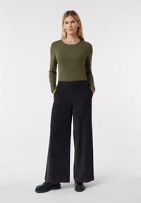 Długi rękaw w oliwkowozielonym kolorze zestawiony z szerokimi czarnymi spodniami. Tkanina o fakturze ze gładkim wykończeniem. Dopasowana w talii, posiada boczne kieszenie.