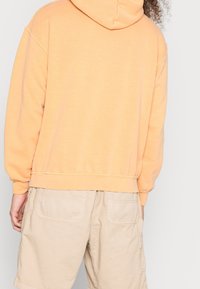 Orange cotton hoodie with a hood and ribbed hem, paired with beige cargo shorts featuring two back pockets. Comfortable and casual fit.