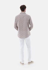 Langärmliges Hemd in Weiß mit einem burgunderfarbenen Blumenmuster; Kragen-Design; getragen mit weißen Hosen und neutralen Sneakers.