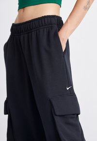 Mustat collegehousut, joissa on joustava vyötärö, sivutaskut ja valkoinen Nike-logo vasemmassa reisissä. Pehmeä kangas ja rento istuvuus.