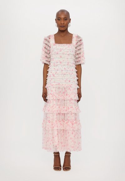 Robe à volants blanche et rose en tissu transparent avec des détails froncés. Encolure carrée et manches bouffantes. Sandales à talons brunes.