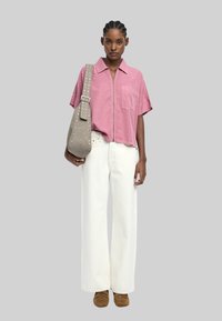 Jasnoróżowa koszula z kołnierzykiem i krótkim rękawem, białe szerokie dżinsy i brązowe zamszowe buty. Torebka z ćwiekami na pasku. Neutralne tło.