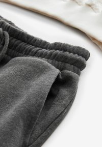 Sivkasta bomba kombiniranega blaga z zloženim pasom; gladka tekstura in rahlo puhasta površina. Nad tem je vidna kremna tkanina.