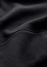 Fekete pamut textil sima, enyhén strukturált felszínnel, finom ráncokkal és varrási részletekkel.