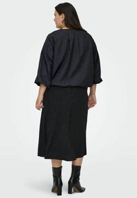 Blusa negra texturizada de corte suelto, combinada con una falda negra hasta los tobillos con sutiles destellos. Calzado: botas negras de tacón.