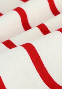 Tessuto di cotone con ampie strisce rosse su un fondo crema, mostrando una texture liscia e un motivo coerente tra gli strati piegati.