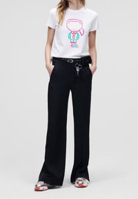 Camiseta blanca con un gráfico de dibujos animados colorido y texto, combinada con pantalones anchos negros con estampado y zapatillas plateadas con detalles en naranja.