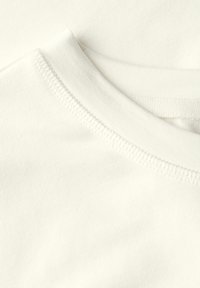 Détail d'un T-shirt en coton blanc, avec un col rond et des coutures visibles. Texture douce avec une finition lisse. Aucun motif ni accent présent.