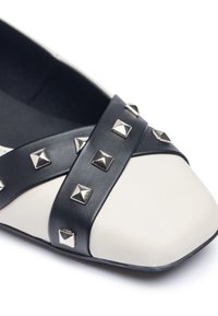 Ballerine in pelle nera e crema con punta quadrata, dotata di una fascia nera decorata con borchie a forma di piramide argentate.