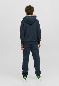 Sudadera azul marino con capucha y pantalones de chándal a juego. Presenta puños y cintura de canalé, además de una textura suave. Combinada con zapatillas blancas.