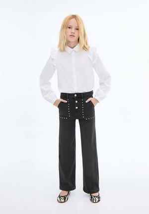 Weißes Hemd mit Rüschensäumen, kombiniert mit hoch geschnittenen schwarzen Jeans mit silbernen Nieten und weitem Bein. Zebra-Print Ballerinas.