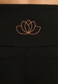 Zwarte legging heeft een gladde textuur met een rosegouden geborduurd lotus bloemen ontwerp op de tailleband, wat zorgt voor een aansluitende silhouet.