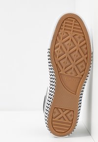 Semelle de sneaker à motif noir et blanc avec une finition en caoutchouc, présentant un dessin de semelle crantée et des accents texturés ; logo de la marque gravé.