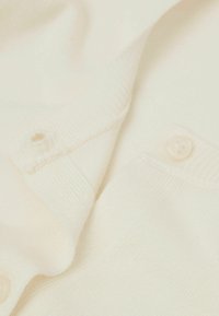 Hellecreme farbener, gestrickter Cardigan mit glatter Textur, gerippten Bündchen und einem einzigen Knopfverschluss. Der Stoff ist weich und leicht.