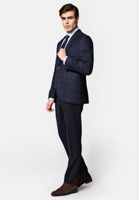 Granatowa marynarka w kratę z brązowymi akcentami, zestawiona z ciemnymi spodniami i brązowymi skórzanymi botkami za kostkę. Posiada zapięcie na guziki i koszulę w paski.