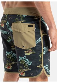 Herren-Schwimmshorts mit einem schwarzen tropikalem Muster und grünen sowie beige Akzenten. Enthält eine beige Gesäßtasche mit Klappe und Ösen-Detail.