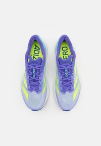 Lila sportcipők hálós felsőrésszel, neon zöld kiemelésekkel, könnyű kialakítással és párnázott talppal a kényelem érdekében.