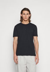 T-shirt preto de mangas curtas feito de algodão macio, com decote redondo e um pequeno logótipo na parte central da frente.