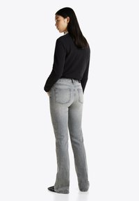 Hallid denim püksid kõrge vöökohaga ja laiade jalgadega, tagaküljel olevate taskutega ja kerge tuhmumisega. Kombineeritud musta pika varrukaga särgiga.