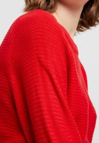 Roter Strickpullover mit einer strukturierten, gerippten Musterung und rundem Ausschnitt; verfügt über lange Ärmel und eine lockere Passform.