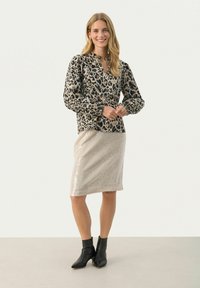 Bluse mit Leopardenmuster, lange Puffärmel, leichter Stoff; kombiniert mit einem taillierten, beige glitzernden Bleistiftrock; schwarze Knöchelstiefel.