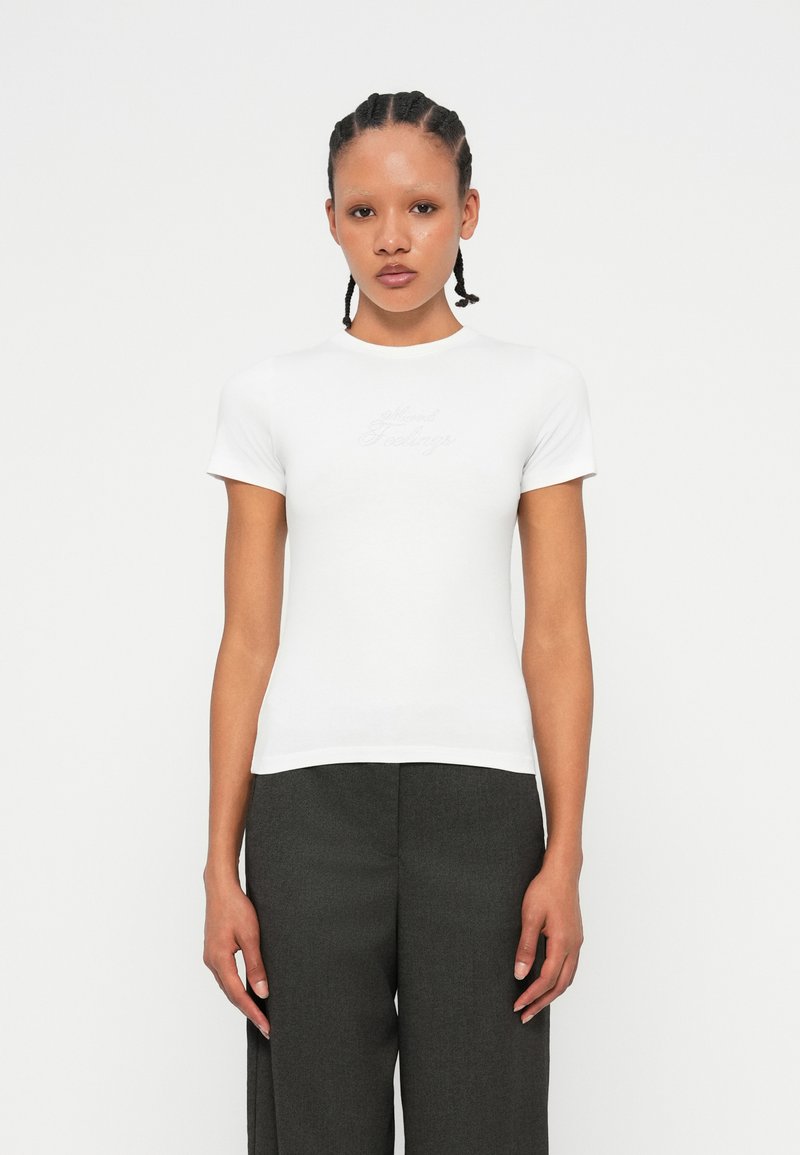 T-shirt bianco fitted in cotone morbido con maniche corte e scollatura rotonda, caratterizzato da un sottile ricamo "Mixed Feelings" sul petto.