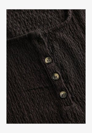 Schwarzes, strukturiertes Stoffoberteil mit rundem Ausschnitt und vierKnopfdetails. Die Knöpfe sind rund und haben jeweils vier Löcher.