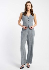 Szary, bezrękawnik z dekoltem w kształcie litery V, pięcioma guzikami i szerokimi nogawkami. Wykonany z teksturowanej tkaniny, zestawiony z czarnymi sandałami na obcasie.