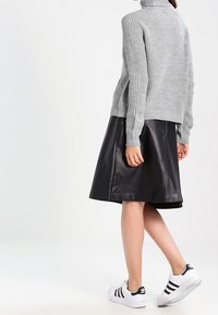 Maglione a collo alto grigio a coste, gonna nera in pelle a trapezio e sneakers bianche con strisce nere. Focus sulla texture e sul contrasto cromatico.