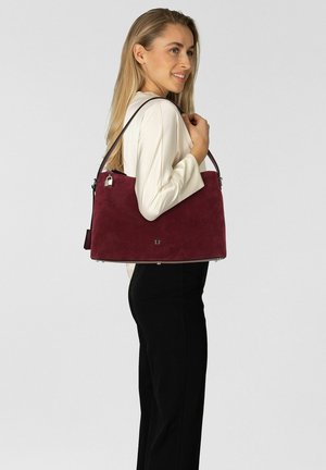 Sac à main en daim bordeaux à la forme structurée, équipé d'une bandoulière amovible, de ferrures argentées et d'un logo discret à l'avant.