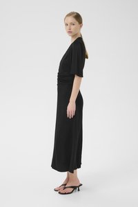 Black maxi dress with a v-neck and short sleeves, featuring side ruching and a smooth texture. Worn with black heeled flip-flops.