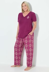 Camiseta morada de cuello en V con un pequeño acento estampado, combinada con pantalones de pijama rosas con un diseño estampado de flores, de corte relajado.