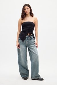 Must mustriba top, millel üksikasjadega ja küljetõmmetega, kombineeritud helesiniste üleliigsete denim teksadega, mis on vabalt istuvad.