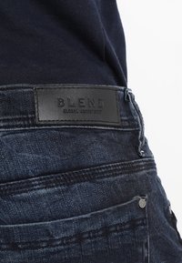 Mørkeblå denimjeans med en teksturert finish, med en svart lærpatch merket "BLEND" på baksiden av midjen og standard lommer.