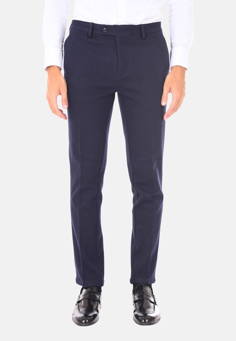 Pantaloni slim-fit blu navy con parte frontale liscia, passanti per cintura e chiusura con un solo bottone, abbinati a scarpe in pelle lucida nere.