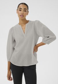 Light gray blouse with a V-neck, puff sleeves, dot texture, and a curved hem, paired with black pants.