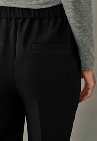 Crne hlače s teksturiranim završetkom, koje imaju elastičnu traku u struku i elegantan dizajn. Sadrže dva mala stražnja džepa.