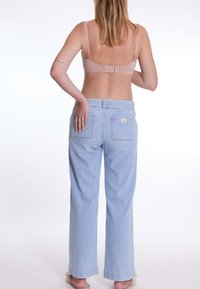 Jeans taille haute bleu clair à coupe décontractée, dotés de deux poches arrière et de coutures décoratives. Portés avec un soutien-gorge beige et des sandales.