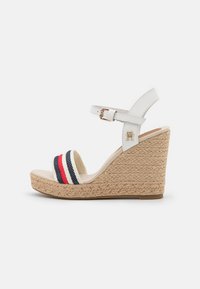 Sandalo con zeppa bianca e suola in juta, caratterizzato da una banda larga a righe rossa e blu navy. Cinturino alla caviglia regolabile con dettagli in oro.