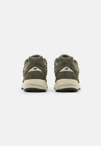 Ett par olivgröna New Balance sneakers sedd bakifrån, som visar perforerat mocka och beige mellansulor mot vit bakgrund.