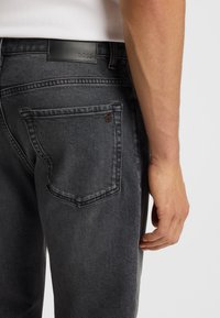 Jeans in denim grigio scuro con un patch in pelle con il logo BOSS, caratterizzati da una tasca posteriore con un sottile accento di marca e una vestibilità affusolata.