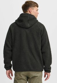 Hoodie en polaire vert foncé avec une finition texturée et moelleuse, des manches raglan et une capuche. Design simple sans matériel ou motifs visibles.