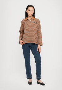 Πολυτελής πόλο με ρίγες σε καφέ αποχρώσεις και ταμπα επένδυση, συνδυασμένο με μπλε τζιν και μαύρες μπαλαρίνες. Το πόλο διαθέτει λογότυπο στο μπροστινό μέρος.