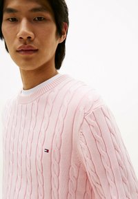 Maglione rosa a maglia rasata con collo tondo a coste e piccolo logo ricamato. Tessuto morbido con motivi verticali in tutto il capo.