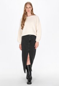 Pulover tricotat crem cu textură pe verticală, asociat cu o fustă din denim negru cu deschidere frontală. Terminat cu cizme negre înalte.
