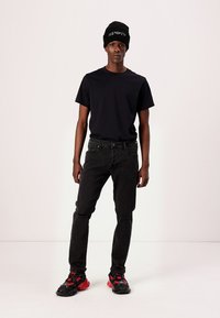 Camiseta negra, jeans desgastados negros, zapatillas negras con detalles rojos y un gorro de punto negro. Conjunto simple y casual.