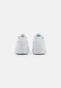 Witte sportieve schoenen met een gladde synthetische bovenkant, geperforeerde details op de hak en een gestructureerde rubberen zool. Eenvoudig, afgerond ontwerp.