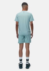 Svetlo modra kratkotrajna športna majica s kratkimi rokavi in usklajenimi hlačami, prikazana s hrbtne strani. Material se zdi lahek z gladko teksturo.
