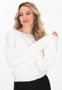 Weißer, gestrickter Pullover mit weitem Halsausschnitt, überschnittenen Schultern und langen Ärmeln. Weiche Textur mit einem gerippten Saumdetail.